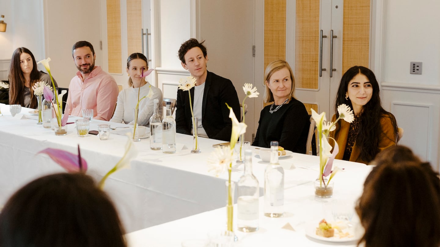 Executives sit at a table with decorative flowers, all turning to the left, presumably to listen to someone speaking.