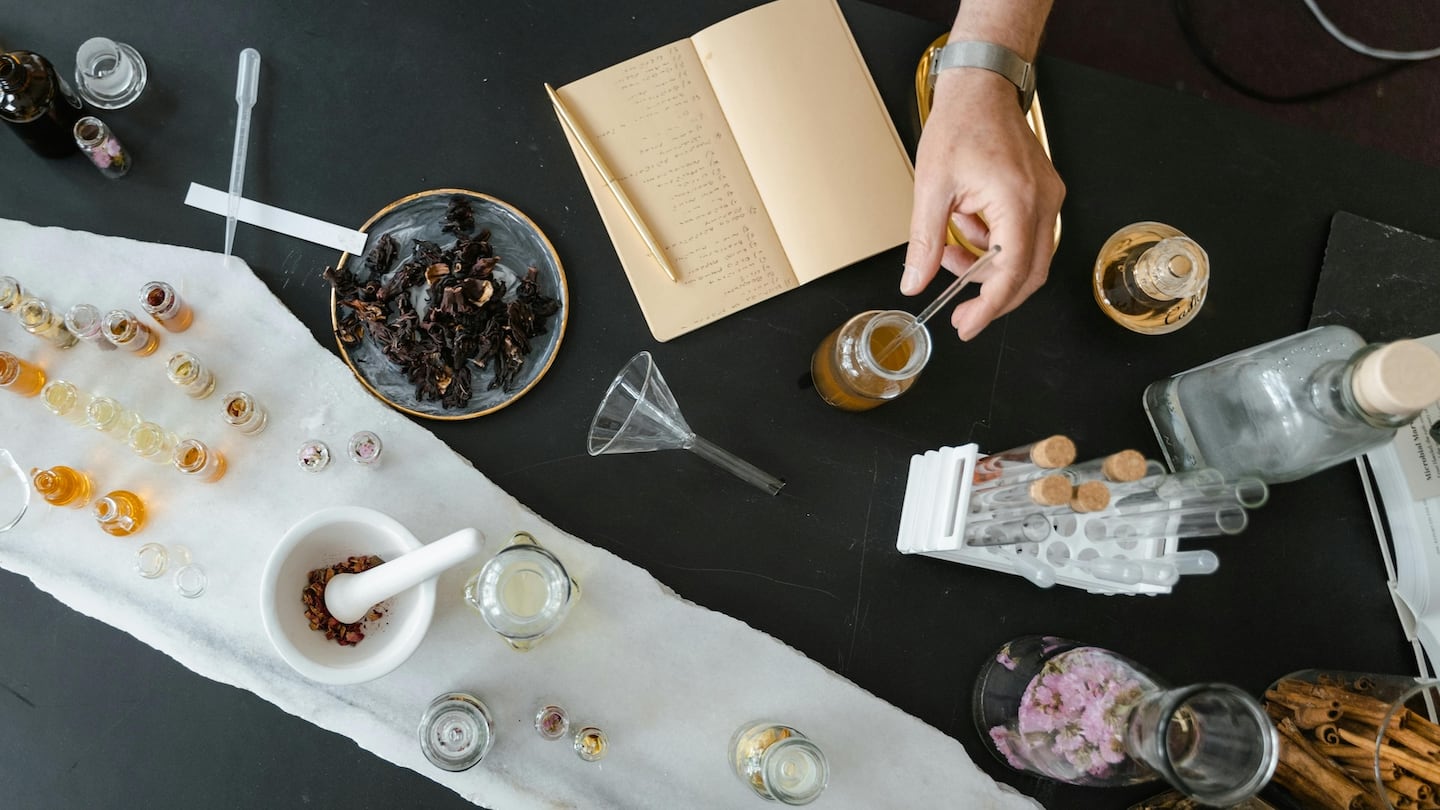 A beauty professional at work. Dried flowers and liquids in containers sit atop a counter, presumably for producing a fragrance.